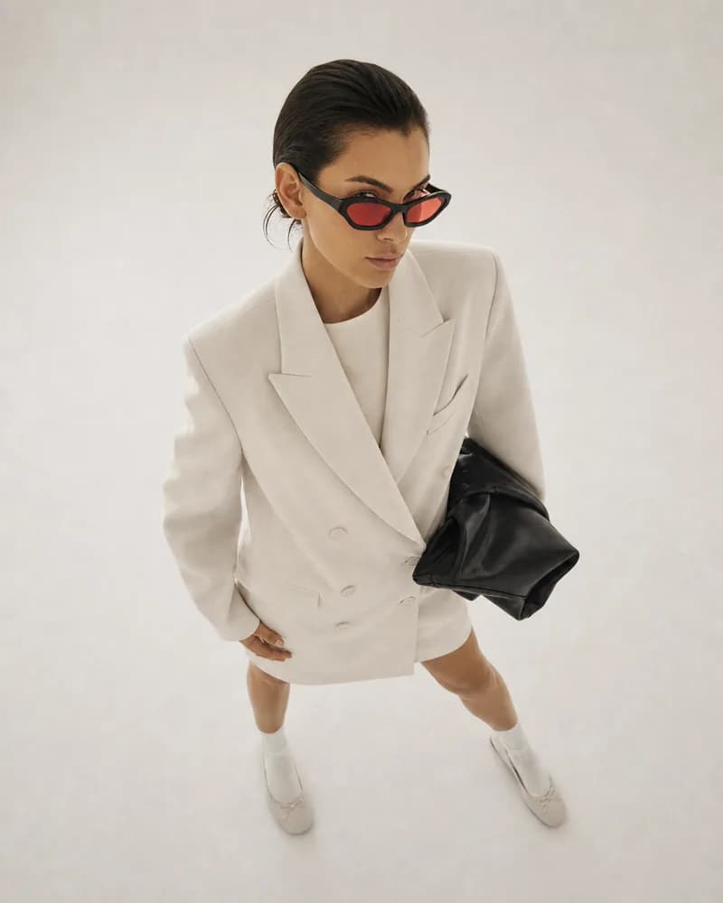 Top-down studio editorial with our model in a cream blazer and black sunglasses