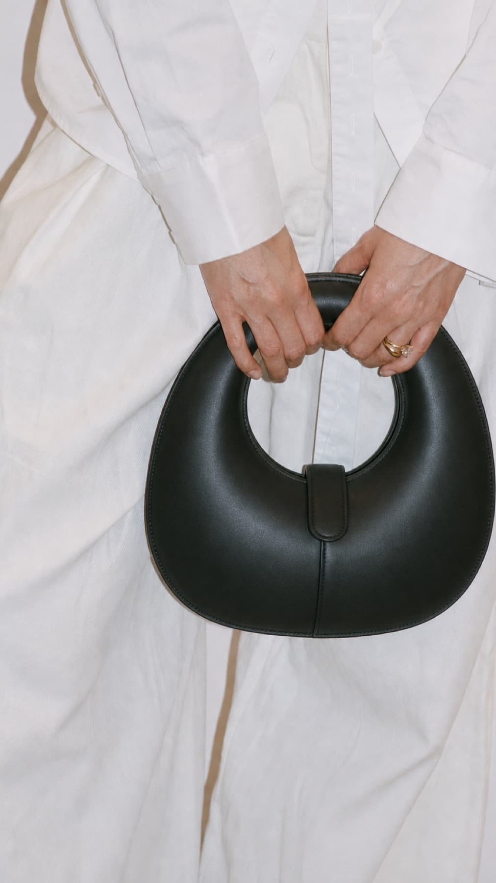 Black sculptural handbag held against white tailoring