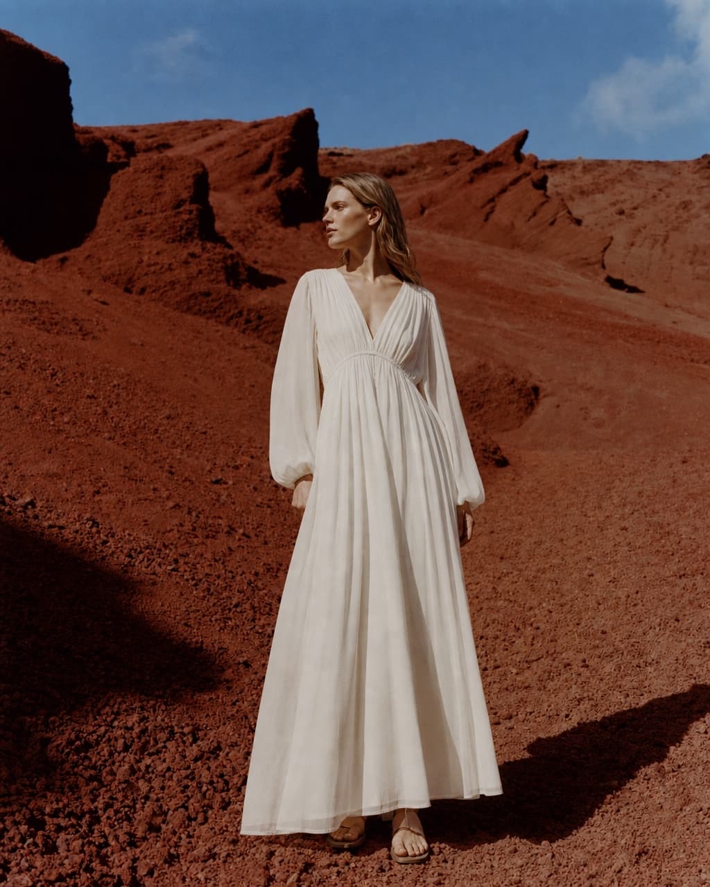 Editorial fashion portrait in a flowing white dress against red earth