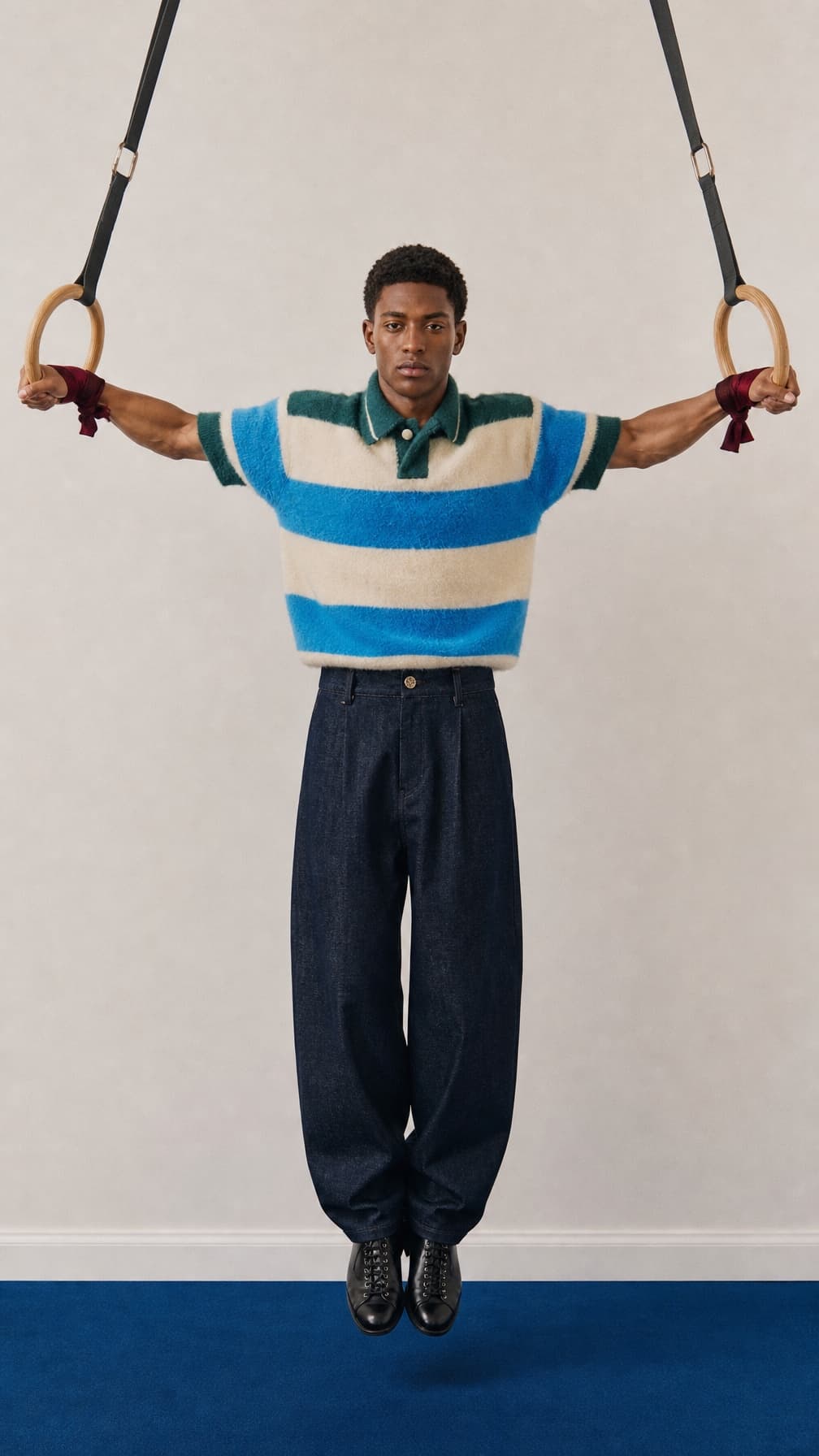Young male model in a striped knit polo suspended from wooden gym rings