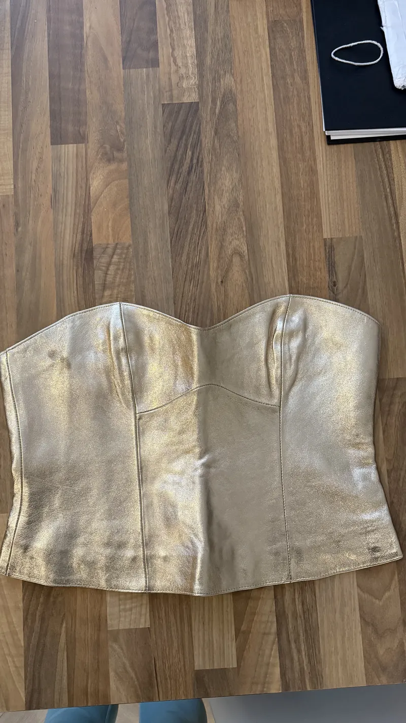 Original product photo: gold corset laid flat on a messy wooden desk