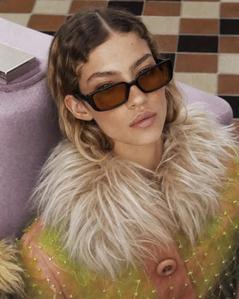 Model in fur collar wearing the sunglasses on a lilac sofa
