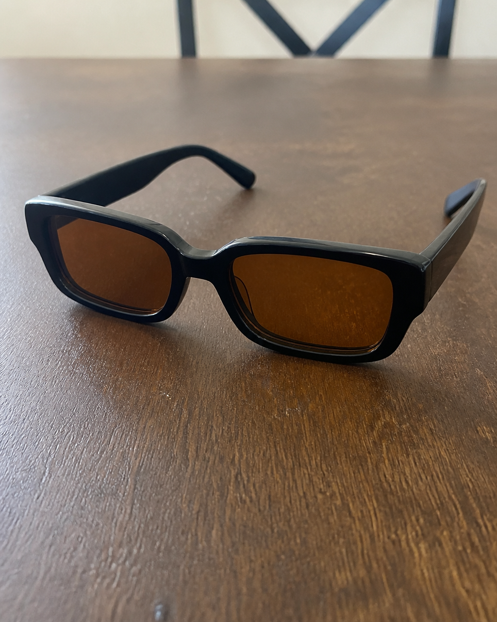 iPhone photo — black rectangular sunglasses with amber lenses on a home dining table